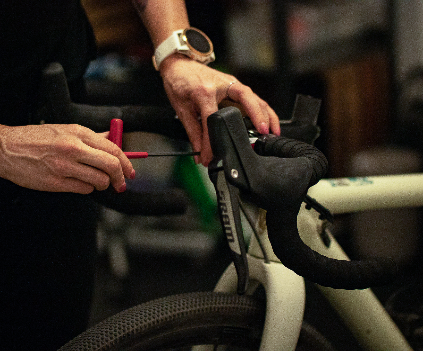 Person adjusting the brake cable on the handlebar of a white bicycle with a red tool.